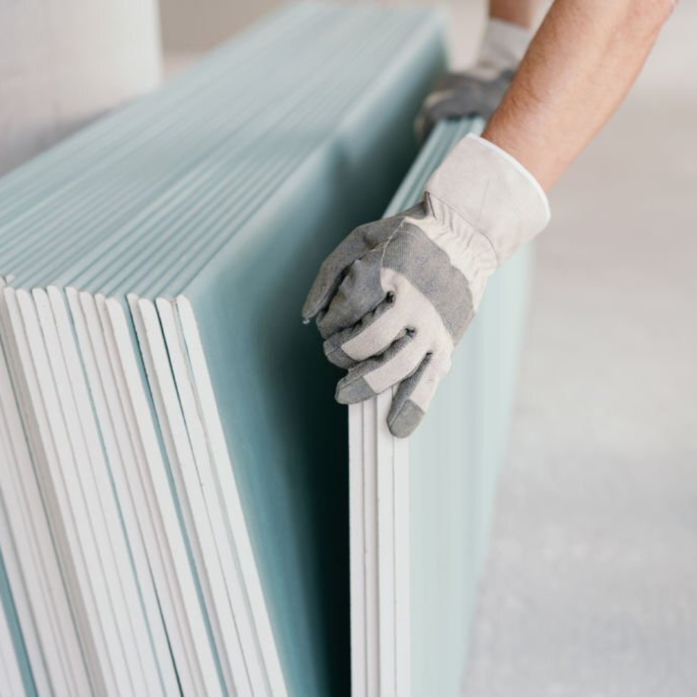 Builder taking a sheet of chip board cladding from a stack against the wall with his gloved hands indoors in a new build home