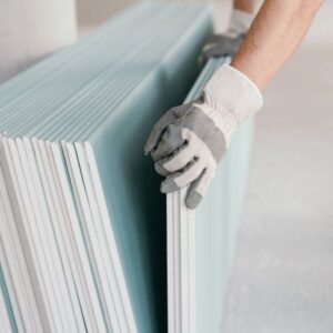 Builder taking a sheet of chip board cladding from a stack against the wall with his gloved hands indoors in a new build home
