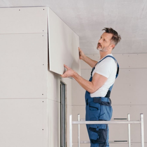 Builder or handyman fitting wall cladding inside a new build house standing on low metal scaffolding