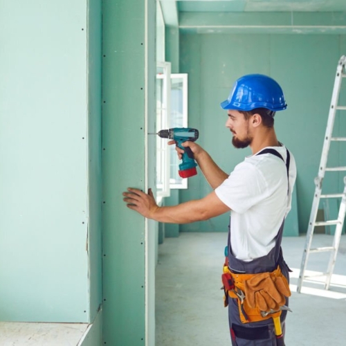 Worker builder installs plasterboard drywall at a construction site office open space. Plasterboard installer.